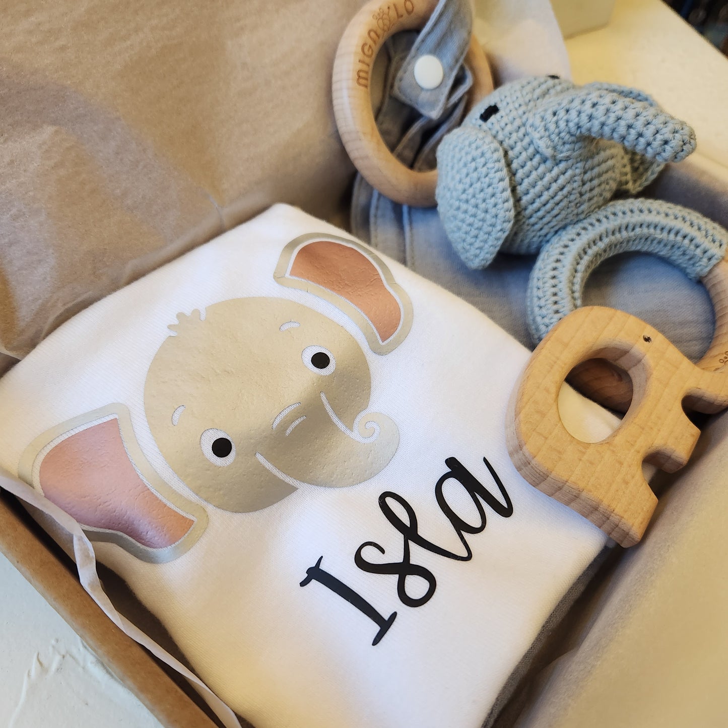Baby blanket with elephant design and text, surrounded by handmade crochet toys on a beige surface
