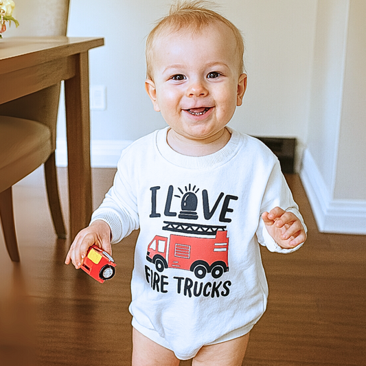 Baby wearing a 'I Love Fire Trucks' shirt holding a toy fire truck indoors.