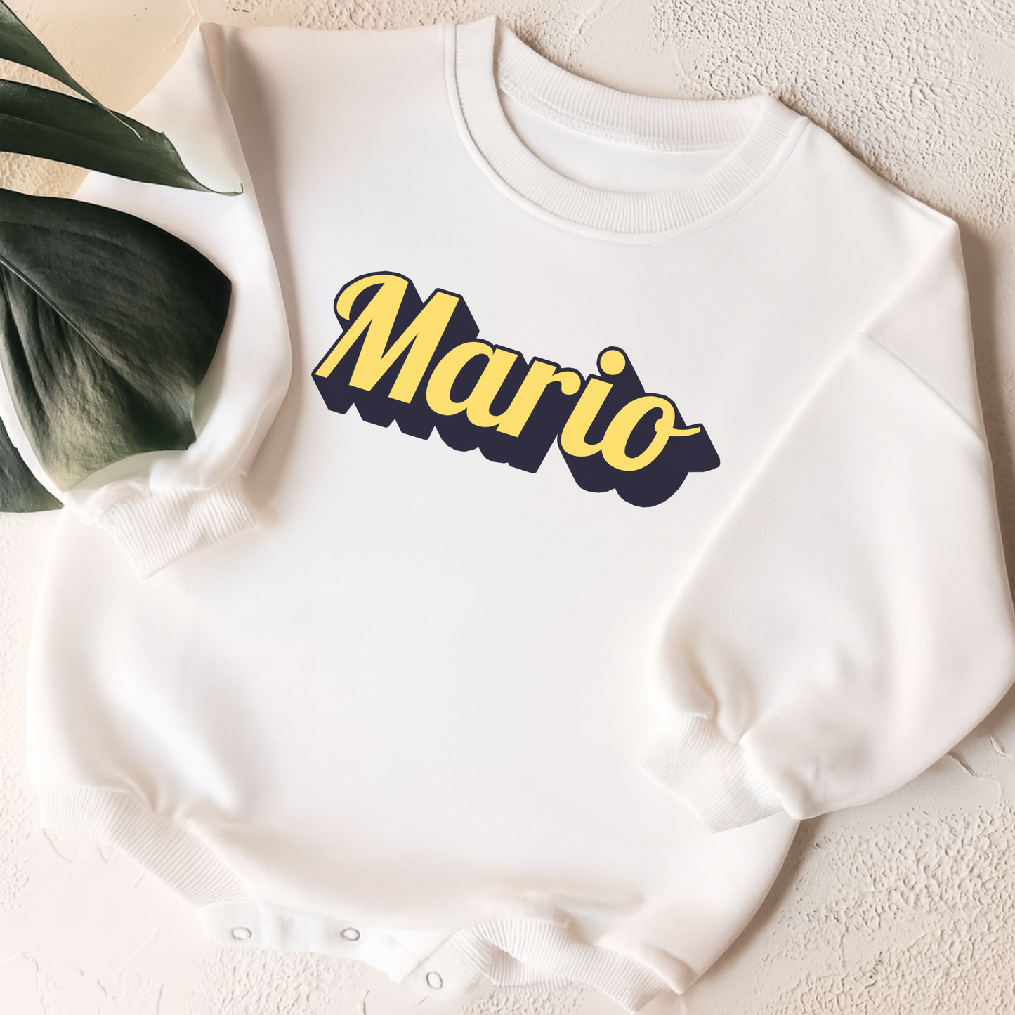 White sweatshirt with 'Mario' printed in yellow and black on a textured surface.