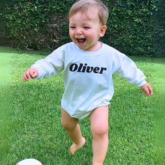Child wearing a shirt with 'Oliver' on it, playing with a ball in a grassy area.
