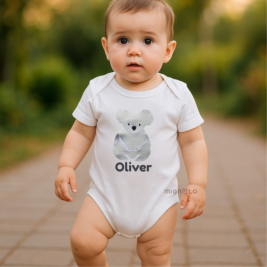 Baby wearing a white onesie with a koala design and the name 'Oliver' outdoors.