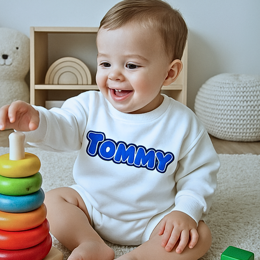 Baby wearing a white shirt with 'Tommy' printed on it, playing with a colorful wooden toy.