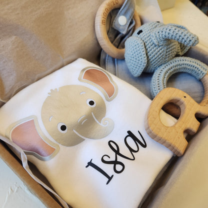 Baby blanket with elephant design and text, surrounded by handmade crochet toys on a beige surface