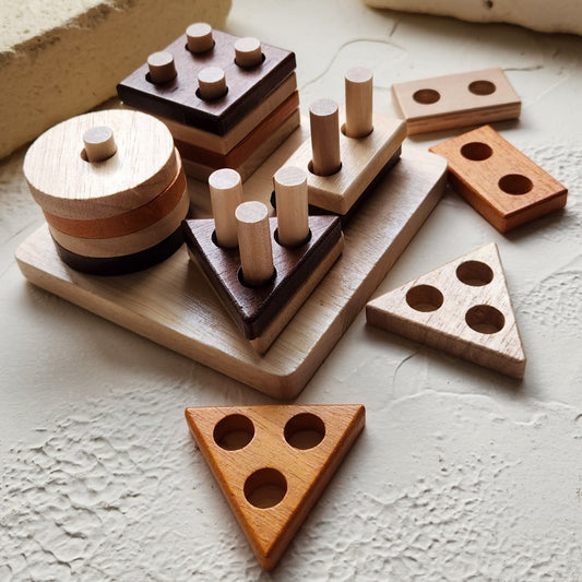 Wooden geometric shapes on a textured wall with blurred greenery in the background