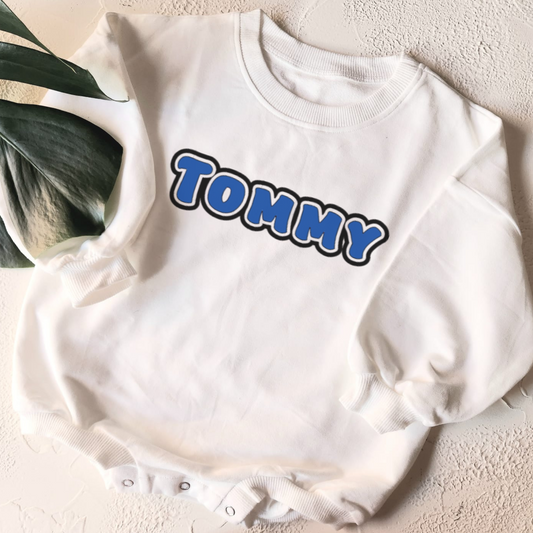 White baby romper with 'Tommy' printed in blue letters on a light background
