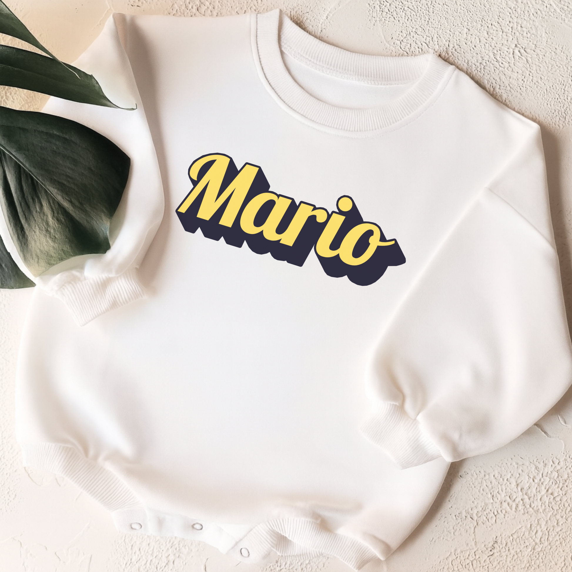 White sweatshirt with 'Mario' printed in yellow and black on a textured surface.