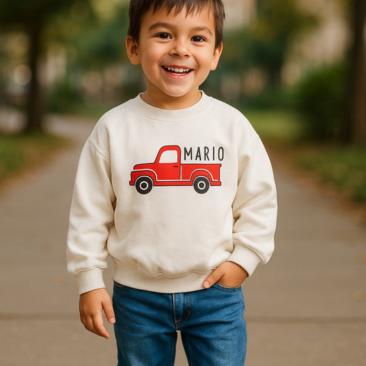 Child wearing a white sweatshirt with a red truck graphic and 'Mario' text, standing outdoors.