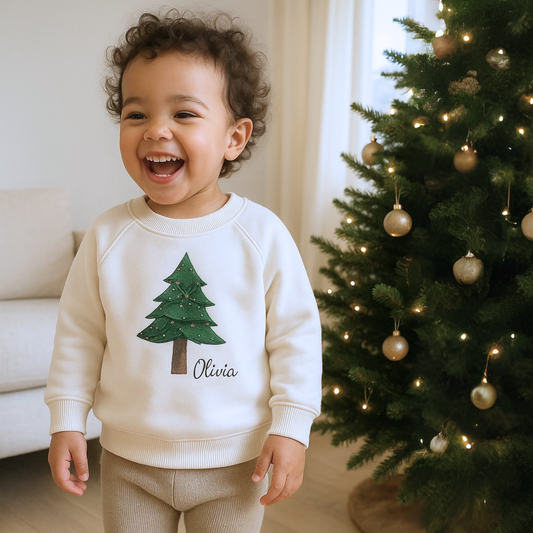 Child wearing a white sweater with a tree design in front of a decorated Christmas tree.