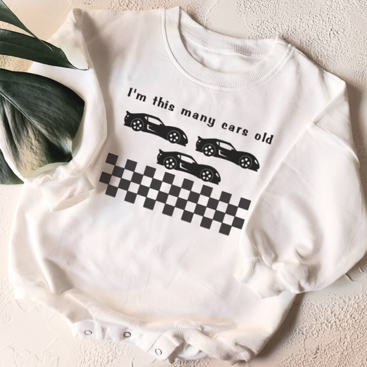 White baby onesie with car-themed design on a light surface