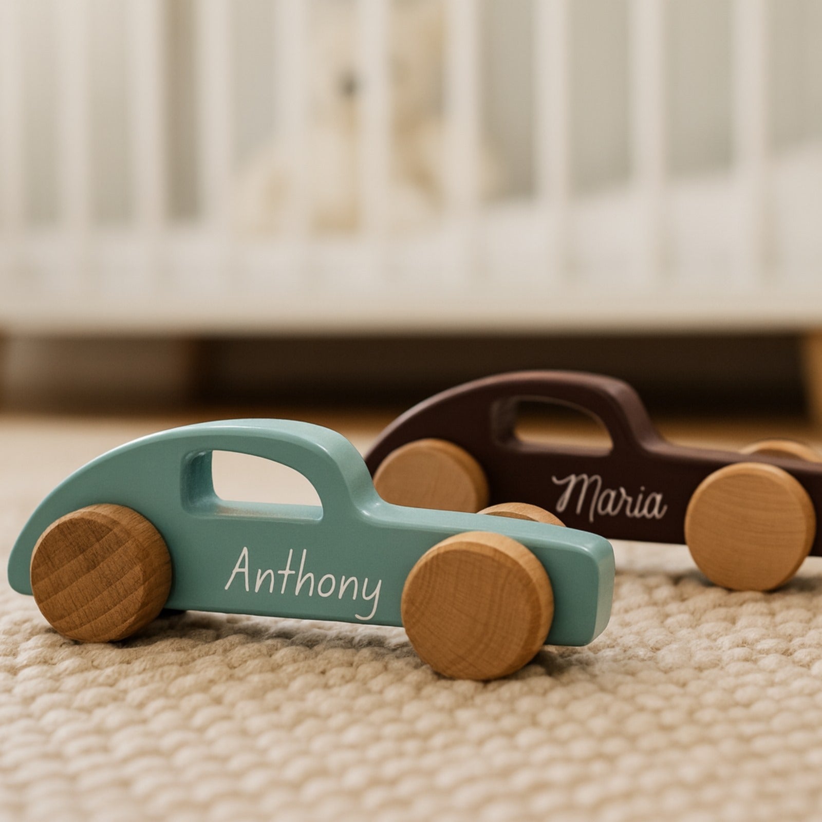 Two wooden toy cars with 'Anthony' and 'Maria' engraved on them, placed on a textured surface.